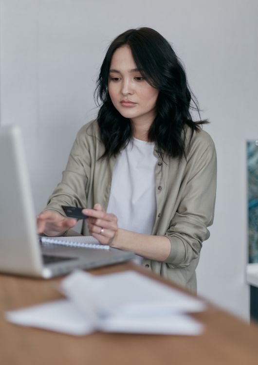A woman holding a credit card while using her laptop.