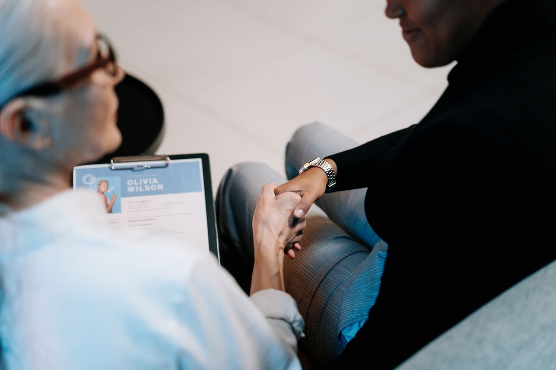 Two people shaking hands across a desk at a job interview.